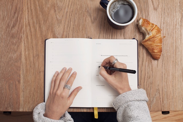 Pessoa a escrever num caderno com café e croissant